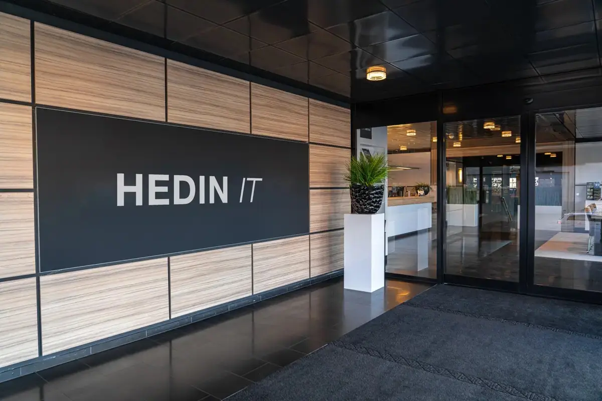 Hedin IT sign on a wood-panelled wall beside the glass entrance doors